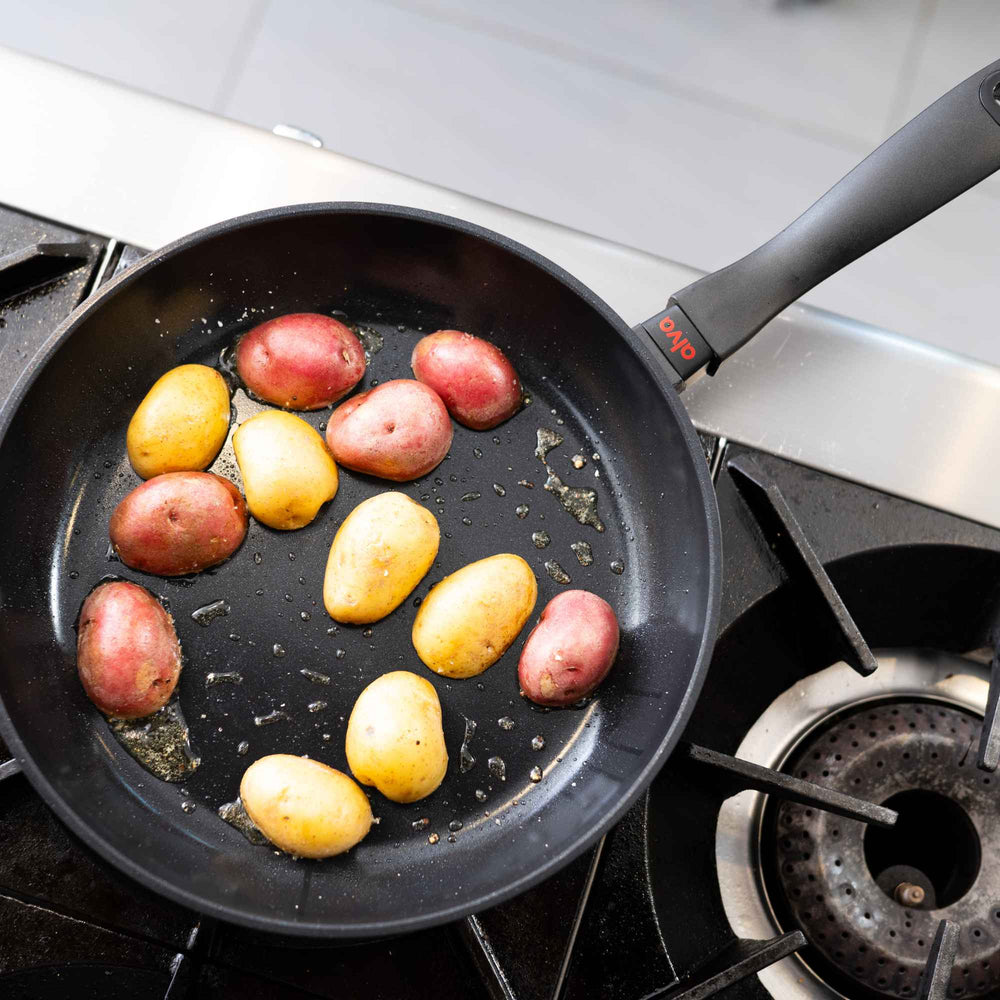 Black nonstick frying pan with small red and yellow potatoes browning on a gas stove