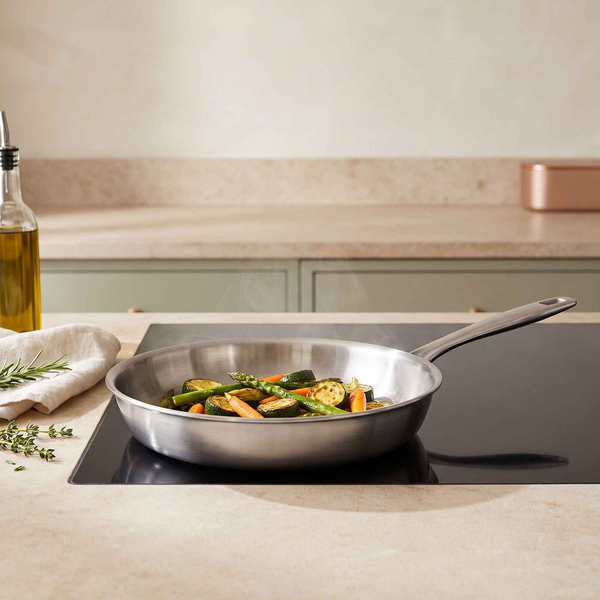 Stainless steel frying pan with sautéed zucchini, asparagus and carrots on an induction cooktop