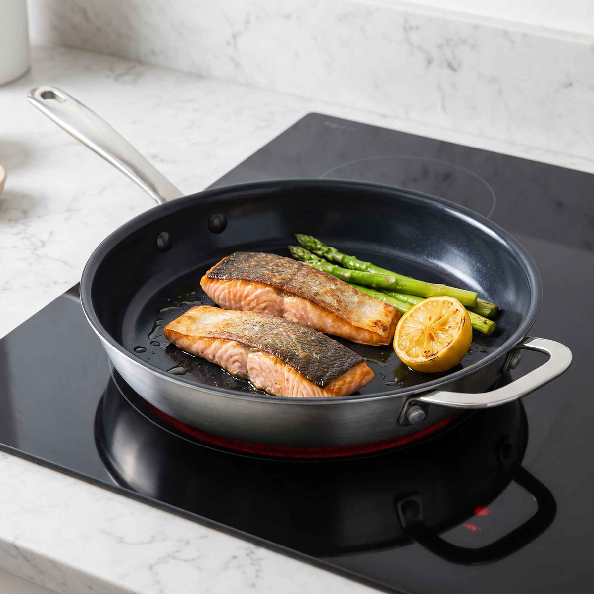 Salmon fillets, asparagus and lemon in an Alva Maestro frying pan with helper handle on an induction cooktop