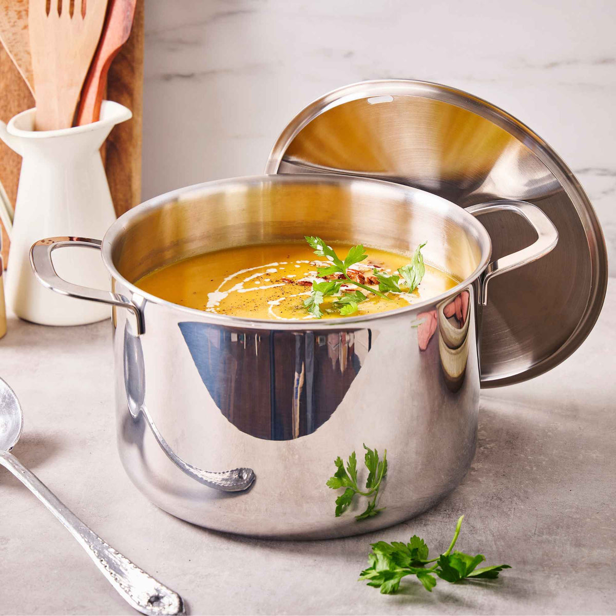 Alva Maestro 5-ply stainless steel stock pot of orange soup with parsley and the lid propped open on a counter
