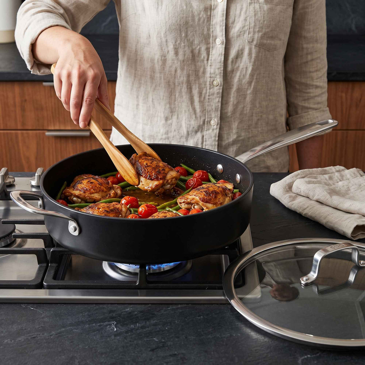 Cooking chicken thighs with cherry tomatoes and green beans in an Alva Maestro ceramic nonstick sauté pan on a gas stove, glass lid beside it