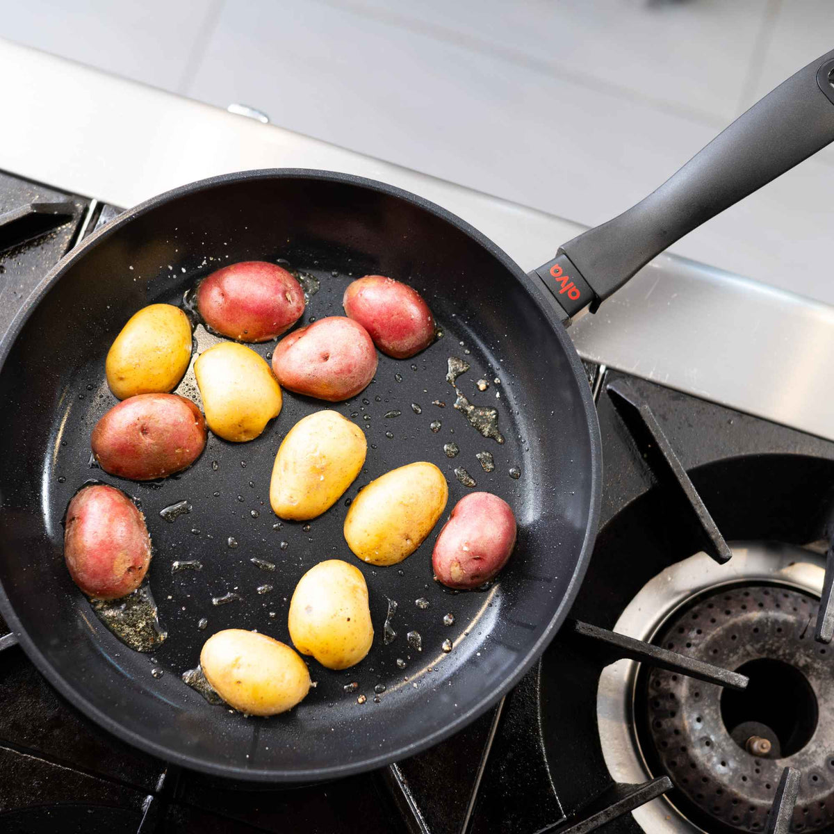 Red and yellow baby potatoes browning in an Alva Energy nonstick frying pan on a gas stovetop