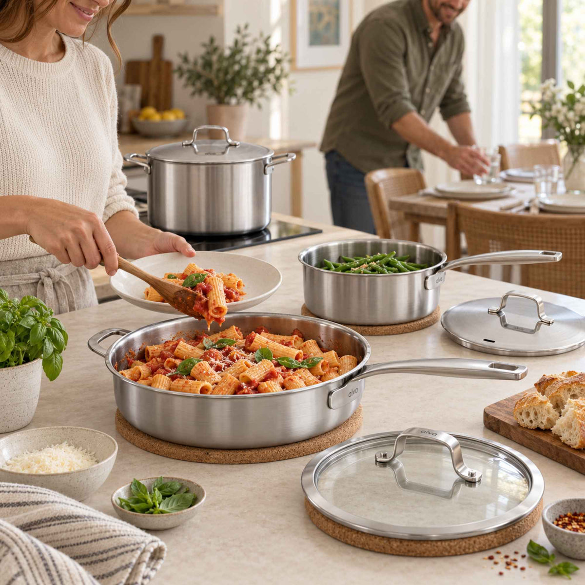 Alva 5-ply stainless steel sauté pan with pasta on the stovetop beside a stockpot and saucepan, couple cooking behind
