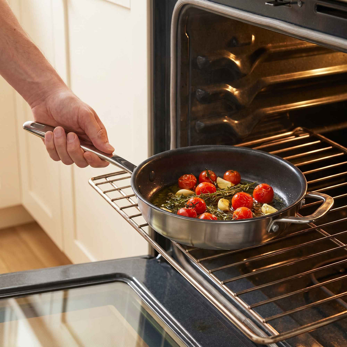 Hand lifting an Alva Maestro frying pan of roasted cherry tomatoes and herbs out of a hot oven