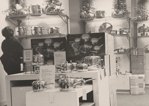 Black and white photo of a kitchenware store display with cookware and sales signs.