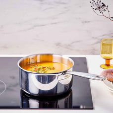 Stainless steel saucepan with orange soup on an induction cooktop with an amber glass nearby