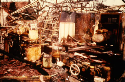 Industrial machines damaged in a fire amidst debris and broken structures.