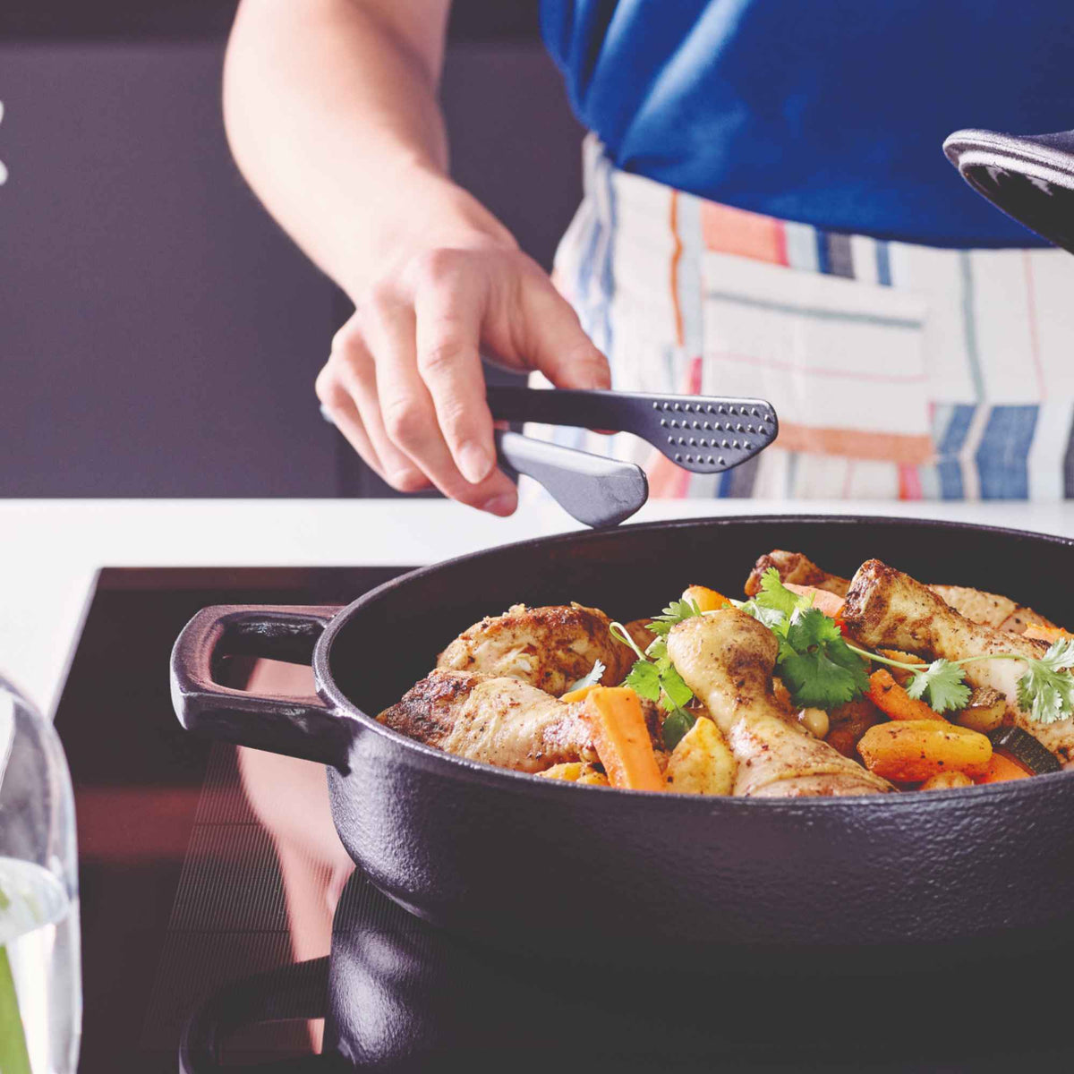 Alva Nori enameled cast iron tagine base with braised chicken and carrots on an induction cooktop, served with tongs