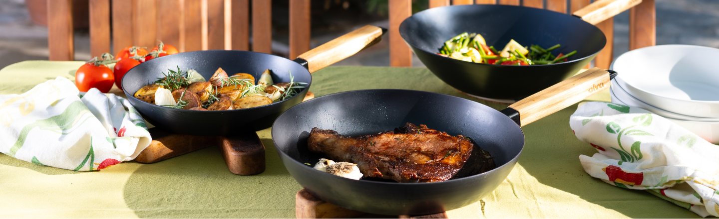 Three pans with diverse dishes on a table, accompanied by fresh vegetables.