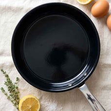 Overhead view of a black ceramic frying pan on a linen cloth with lemon, thyme and eggs