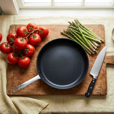 Alva Maestro ceramic nonstick frying pan on a cutting board with tomatoes, asparagus and a chef's knife
