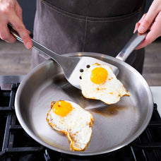 Fried eggs on a slotted spatula in an Alva Maestro 5-ply stainless steel frying pan on a gas stove