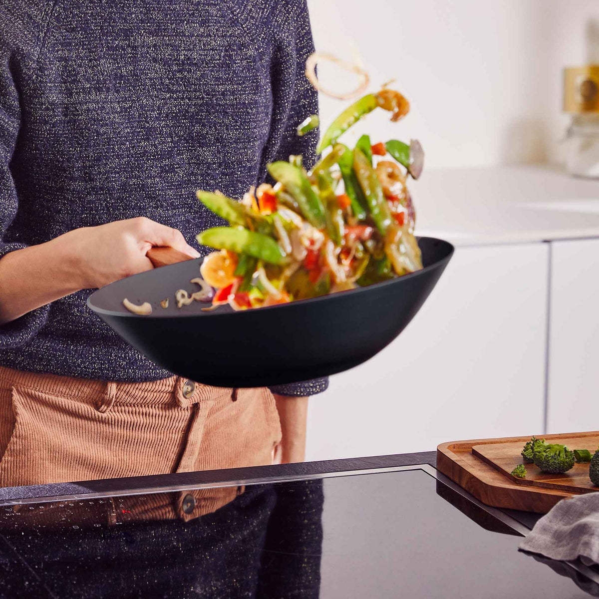 Person tossing stir-fried vegetables in an Alva Forest carbon steel wok in a bright kitchen