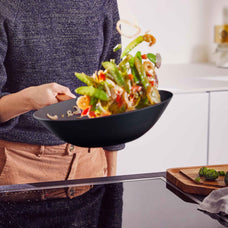 Person tossing stir-fried vegetables in an Alva Forest carbon steel wok in a bright kitchen
