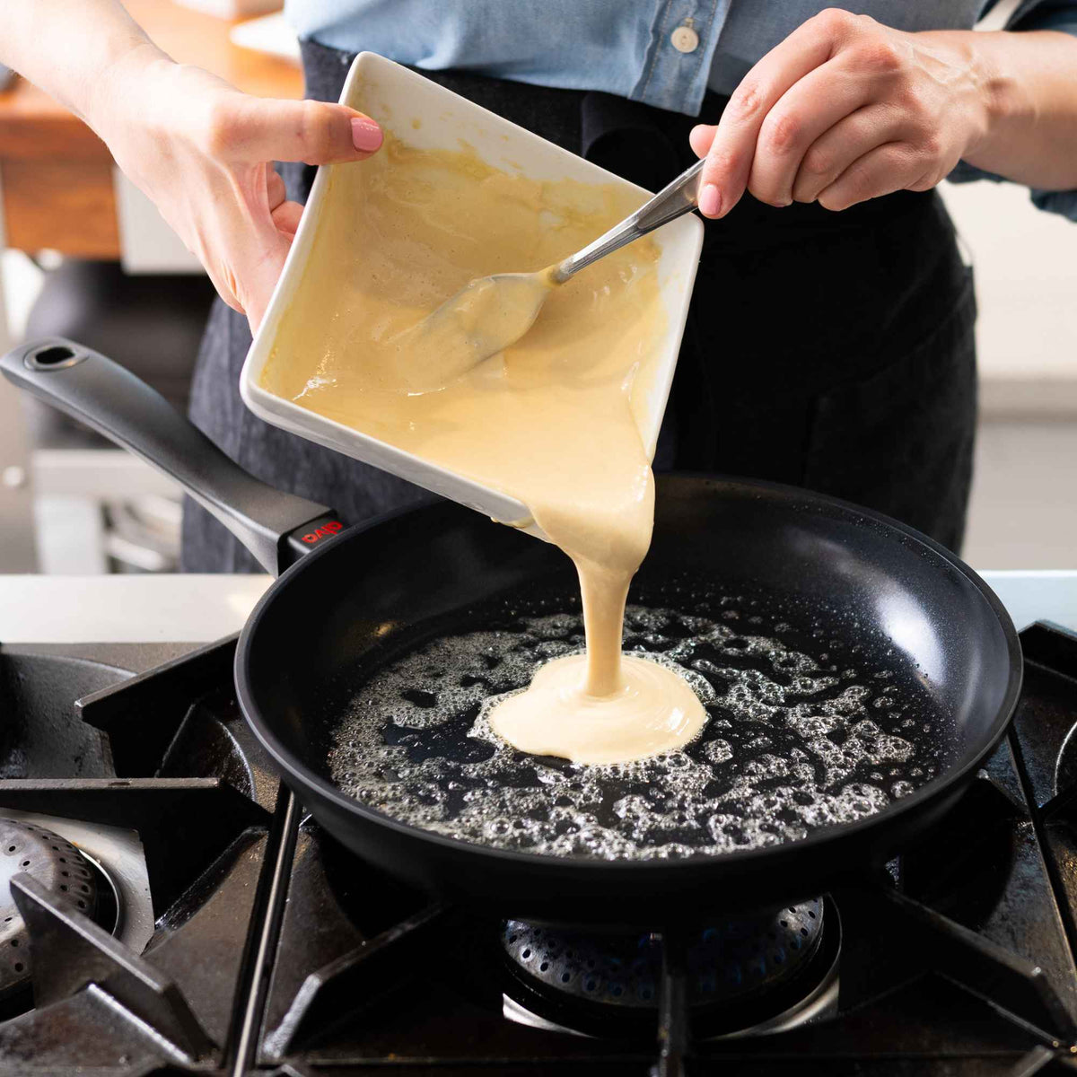 Pouring batter into an Alva Energy nonstick frying pan with hot oil on a gas stovetop