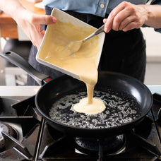Pouring batter into an Alva Energy nonstick frying pan with hot oil on a gas stovetop