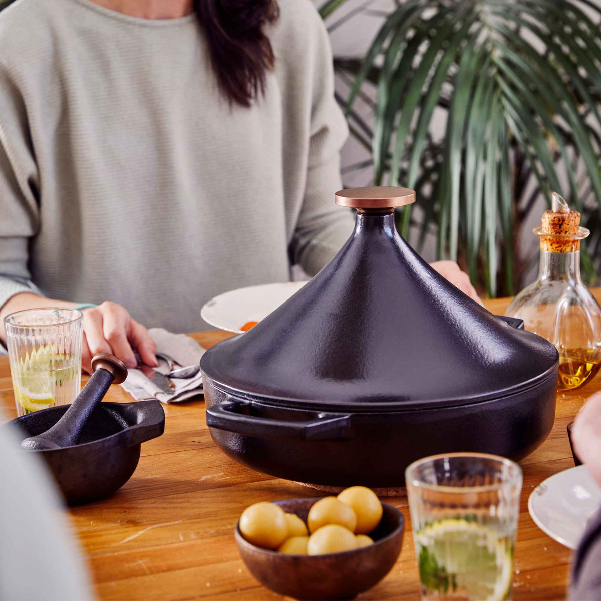 Alva Nori black enameled cast iron tagine with copper-tone knob on a wooden dining table with lemons and herbs