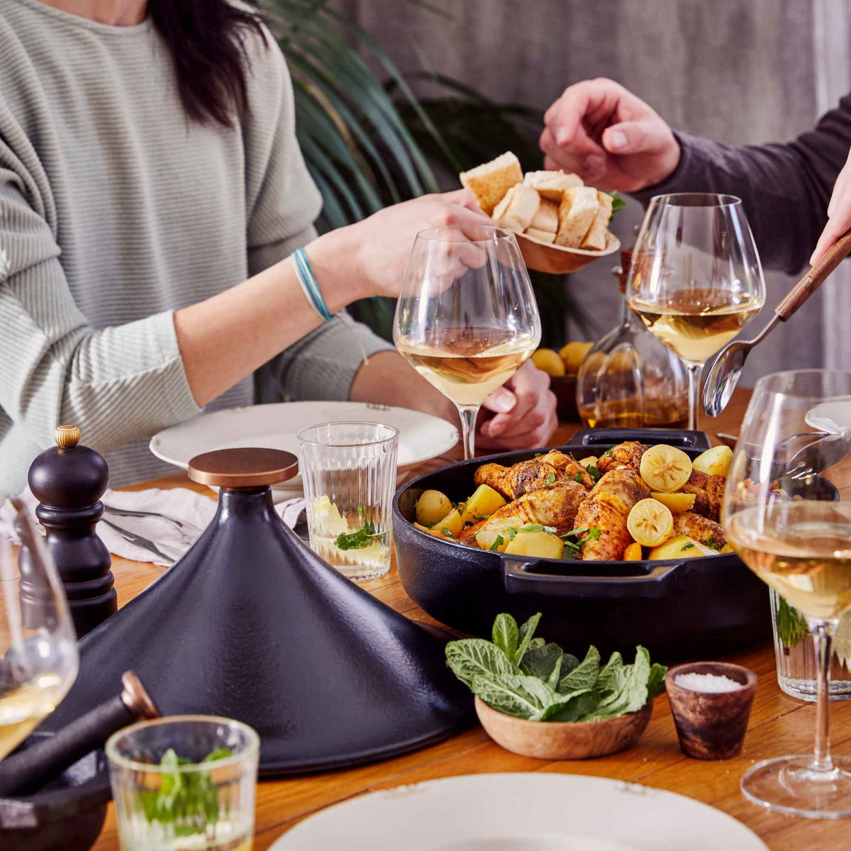 Friends sharing a chicken and potato meal served from an Alva Nori enameled cast iron tagine at a dinner table