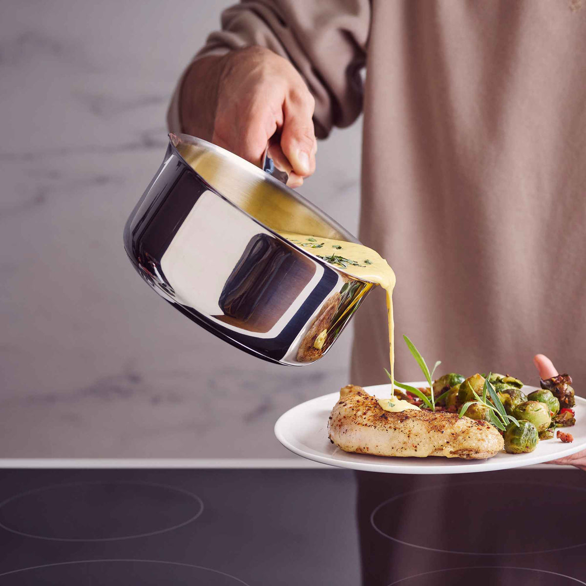 Pouring sauce from an Alva Maestro 5-ply stainless steel saucepan over roast chicken and Brussels sprouts