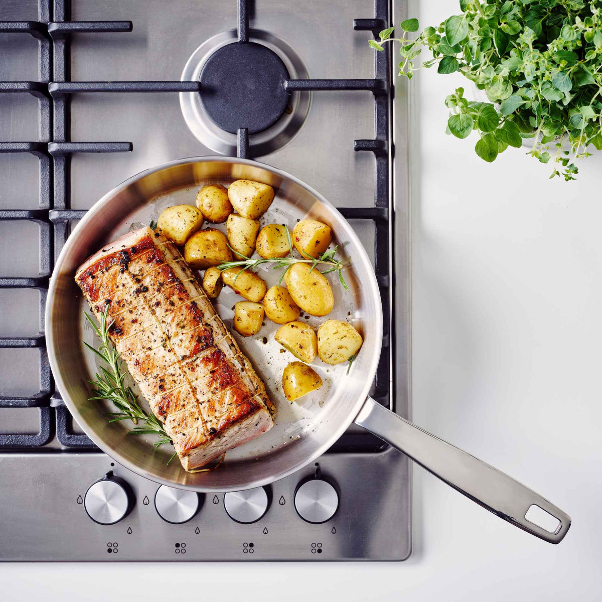 Overhead view of pork loin and roasted potatoes in an Alva Maestro 5-ply stainless steel frying pan on a gas cooktop