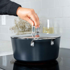 Hand holding the stainless lid of an Alva Maestro ceramic nonstick stock pot on an induction cooktop