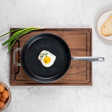 Overhead view of an Alva Maestro 5-ply ceramic nonstick frying pan with a fried egg on a walnut cutting board