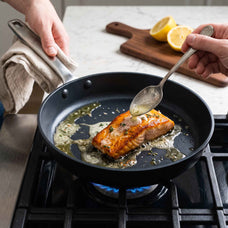 Spooning butter sauce over a salmon fillet in an Alva Maestro ceramic nonstick frying pan on a gas stove