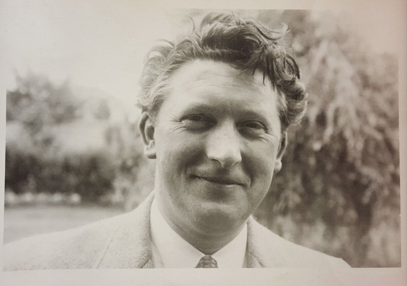 Smiling man with curly hair in a suit, outdoor background.